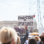 Man holding a sign which reads "education = opportunity".