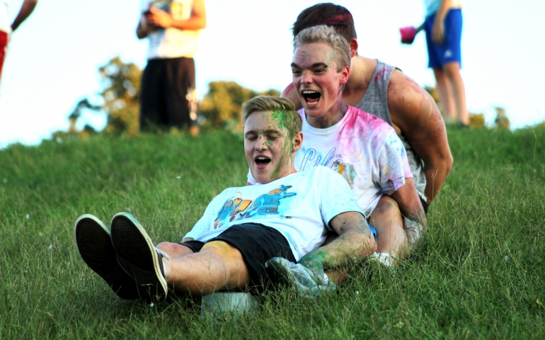 Three male students sliding down the hill on one block of ice