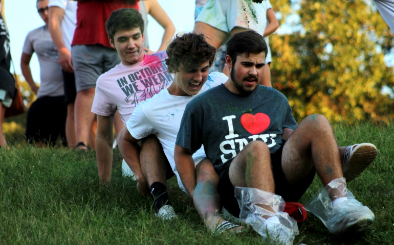 Three male students sliding down the hill on a block of ice together