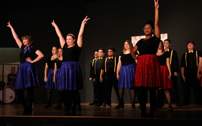 A cast of men and women posing while singing