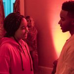 A man and a woman in a red lit room talking to one another