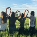 4 women standing in a field linking their arms together
