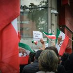 A snapshot of a protest over Mahsa Amini's death, a central poster reading "Woman, Life, Freedom"