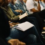 A group of faceless individuals seated in an audience